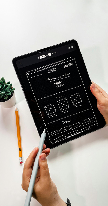 Personne dessinant un design web filaire sur une tablette avec un stylet.